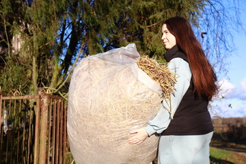 a girl in the village is carrying fresh hay to feed pets
