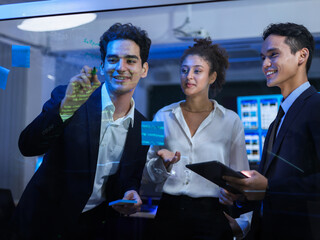 Multi-ethnic team of business professionals is actively collaborating on transparent glass board with sticky note. Strategy development and technology brainstorming. Project meeting at the office