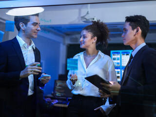 Multi-ethnic team of business professionals is actively collaborating on transparent glass board with sticky note. Strategy development and technology brainstorming. Project meeting at the office