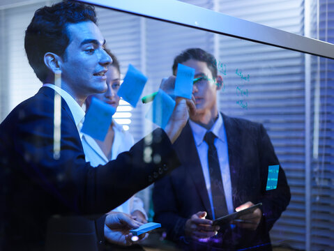 Professional team collaborating on a transparent screen in a futuristic. Writing with sticky notes and technology for strategic planning, innovative development, and successful project analysis