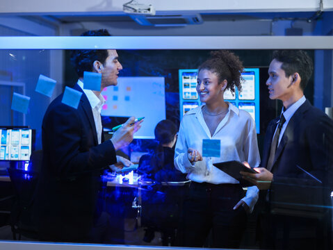 Diverse team of business collaborating and brainstorming project showing idea on glass board with sticky notes and digital tools. Successful innovation, digital transformation, problem-solving