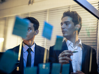 Business team collaborating tech office, strategically utilizing a glass whiteboard and sticky notes to visualize data and brainstorm innovative ideas. Corporate teamwork, planning strategy
