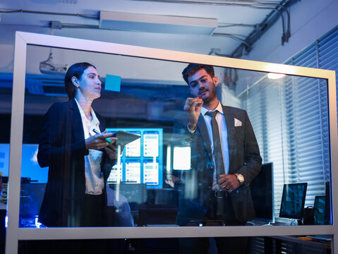 Two diverse business team collaborate in the office, brainstorming and writing on a transparent glass whiteboard. successful teamwork, innovative IT solutions, corporate planning for a startup company - Powered by Adobe