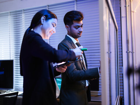 Two diverse business colleagues in collaborative teamwork in the office. Brainstorming and writing ideas on a glass whiteboard. Successful partnership for tech development or corporate strategy plan