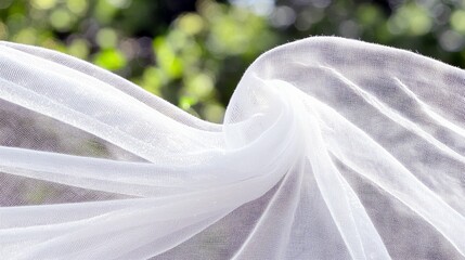 Close-up of white fabric billowing in the wind, with a blurred green background of leaves and sunlight.