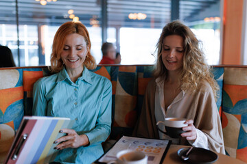 Businesswomen engage in conversation over coffee at a modern cafe while reviewing documents and enjoying each other's company in a vibrant setting