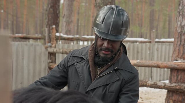 man checks horse equipment, male inspecting gear in barn, individual examines tack amidst snowy stable environment, man with helmet reviews horse equipment inside winter barn setting