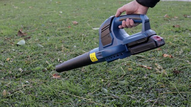 Cordless leaf blower moving scattered leaves across grass surface