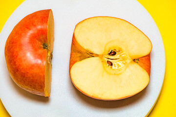 The apple on the white plate is cut in half with a knife