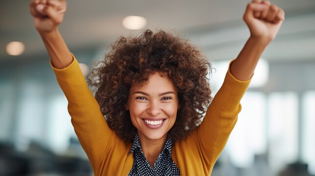 In a bright office space, a cheerful woman with curly hair raises her arms in triumph. Her smile radiates joy, celebrating a personal achievement during the day