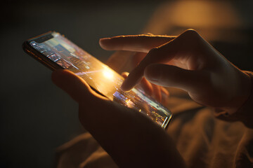 Close-up of a person using a smartphone in a dark room with city lights reflecting on the screen