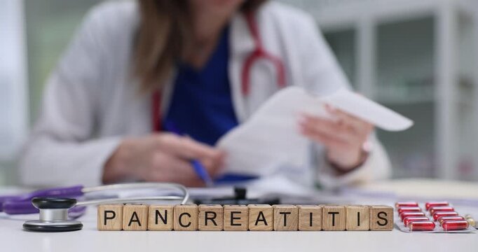 Doctor examines ultrasound images of pancreas of patient. Wooden cubes arranged neatly on table form word Pancreatitis symbolizing suspected diagnosis