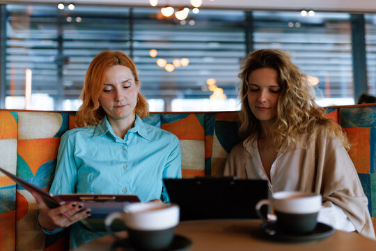 Businesswomen discussing plans while reviewing a menu in a modern cafe during a casual meeting in the afternoon
