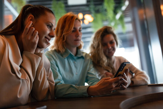 Three businesswomen engage in a discussion while reviewing a smartphone in a modern office space during early afternoon