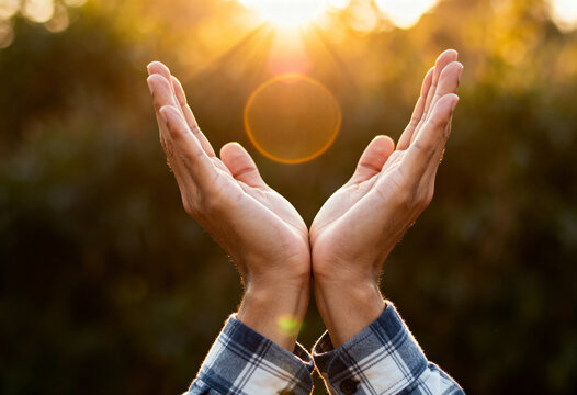 Hands cupped open facing bright sun with lens flare in outdoor setting representing hope and nature connection