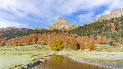 A scenic view of a mountain range with a river flowing through a valley surrounded by autumn trees