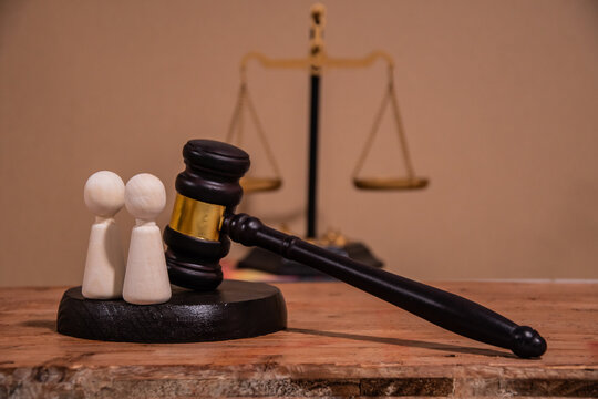 A judge's gavel and scales of justice stand next to two wooden figures symbolizing a judicial decision regarding civilians