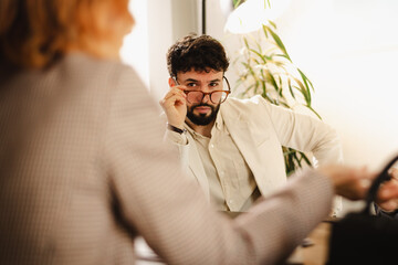 Business meeting in office with a focused man in a suit observing a woman presenting ideas during the afternoon session in a modern workspace