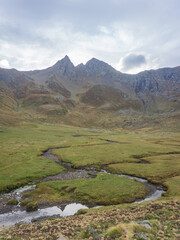 Mountain landscape with a stream winding through a green valley under an overcast cloudy sky view outdoors