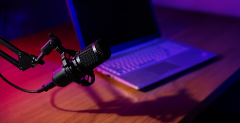 podcast recording, streaming and broadcasting. microphone with laptop on the table in studio with neon lights. banner with copy space