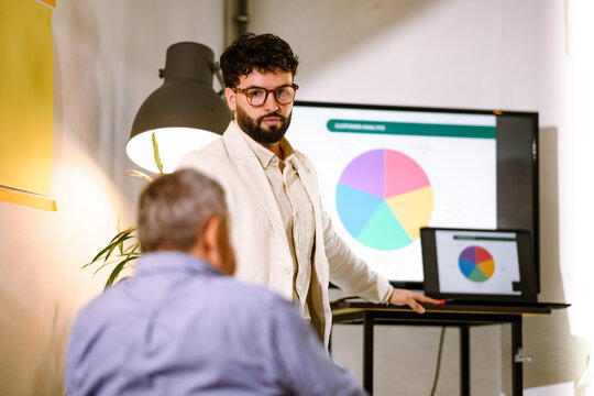 Business presentation in a modern office setting with a young presenter discussing pie chart data to engaged audience member