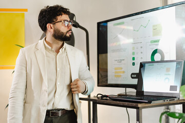 Professional man presenting business data with graphs and charts during a meeting in a modern workspace with a laptop and projector setup