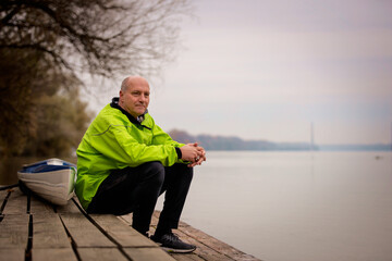 Sporty active senior sitting on the jetty by the river next to his kayak