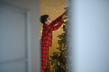 Boy decorating christmas tree wearing pajamas during holiday season