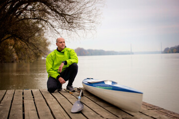 Sporty active senior sitting on the jetty by the river next to his kayak