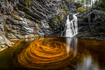 Floating autumn leaves swirl in the pool below Lower Cascade Falls, a waterfall in Hanging Rock State Park in Sauratown Mountains of North Carolina.