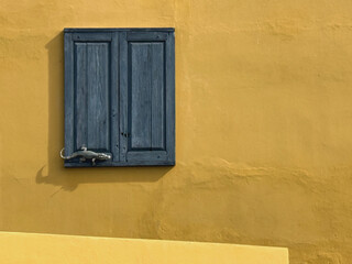 Fenster mit blauen Fensterläden an einer gelben Fassade