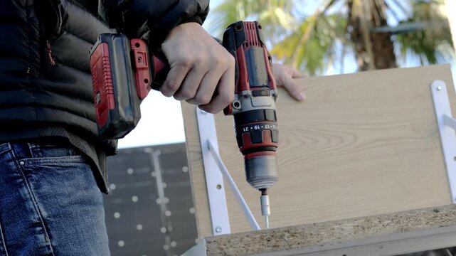 Battery-powered drill securing bracket to wooden board corner from side angle