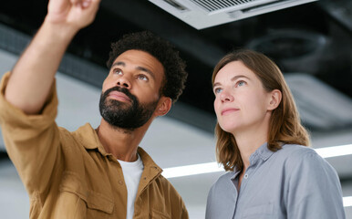 Professional diverse couple looking focused while inspecting new ceiling air conditioner cassette installation inside modern commercial building office space