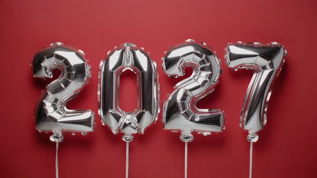 Silver &ldquo;2027&rdquo; balloons on strings against red background symbolizing festive energy and milestone celebration