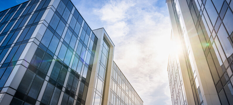 Low Angle Shot Of Modern Glass And Steel Corporate Office Buildings Under A Bright Blue Cloudy Sky