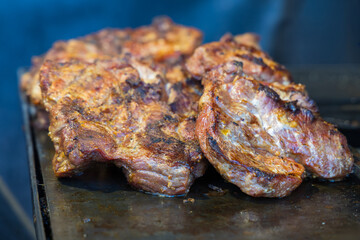 A macro detailed shot of several slices of grilled pork neck placed on a hot metal griddle or flat top grill. The meat has dark, seared edges and a golden-brown surface with visible seasoning