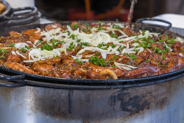 A detailed shot of a huge cast-iron pan or wok filled with chunks of meat in a dark, thick sauce likely chicken or pork ragout. The dish is richly glazed and has a shiny, caramelized appearance