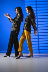 Stylish twin sisters showcase modern fashion against a vibrant backdrop in urban setting