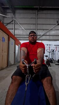 Video of a plus size man exercising on a rowing machine at the gym. The scene captures focus, strength, and determination during a real workout routine under artificial light.