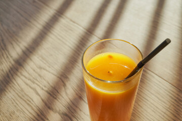 Sea buckthorn fruit drink with black straw in glass on wooden table