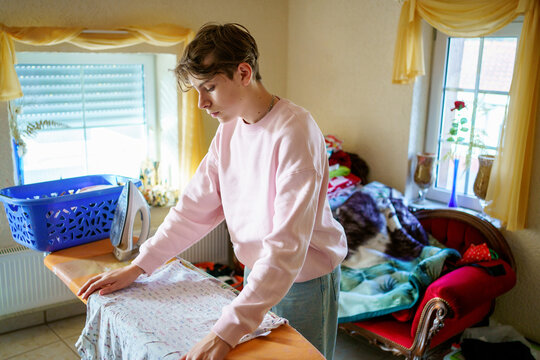 Teenage boy doing and ironing laundry at home with an iron
