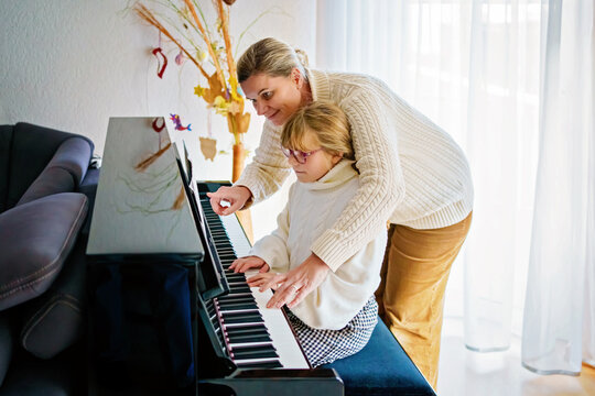 Little girl playing piano at home. Happy child practices music instrument with mother.