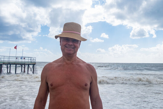 mature bald man straw hat smiling beach waves ocean background, summer vacation lifestyle, happy active retirement, health retired man, positive senior, sun protection, cheerful senior man smiling