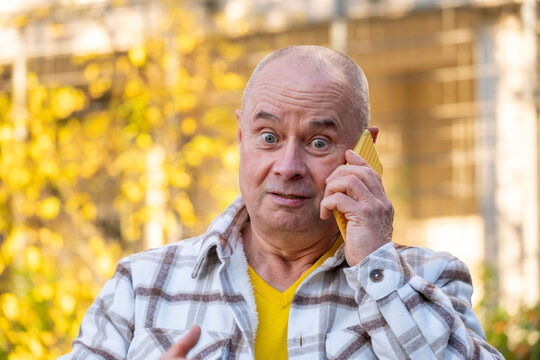 Elderly man holding yellow phone to ear, looking directly camera with thoughtful expression outdoors, senior uses smartphone in garden, modern connectivity and active aging, moment communication