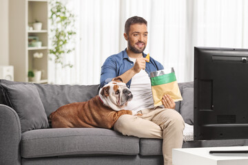 Man eating crisps on a sofa with a bulldog
