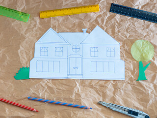 Paper house sketch with craft tools on crumpled kraft paper background, creative architectural concept
