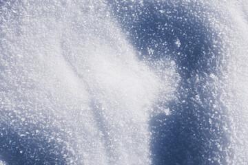 Winter holidays. Close-up of fresh sparkling snow under bright sun. Textured winter background with soft white drifts and deep blue shadows for contrast