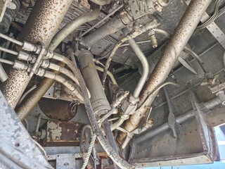 Close-up of numerous rusted hydraulic pipes, fittings, and cables underneath an old aircraft or...