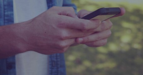Tapping pair of adult hands using smartphone at park, with denim shirt and white T-shirt