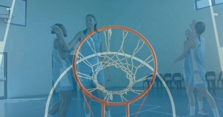 Framing close-up rim and white net, teammates high-fiving on gym court wearing light-blue jerseys